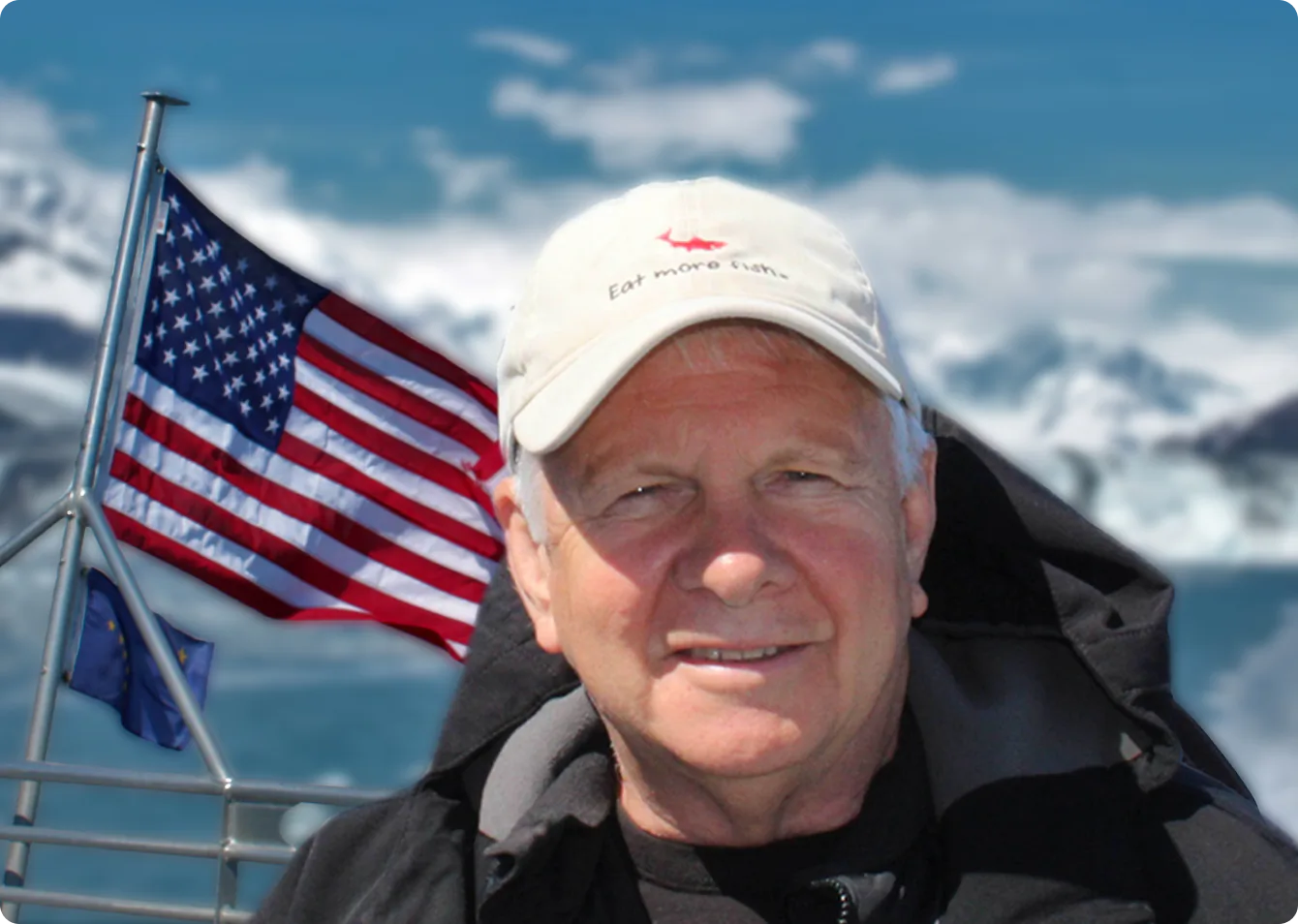 Gregg Brelsford with American and Alaska flags against mountain backdrop